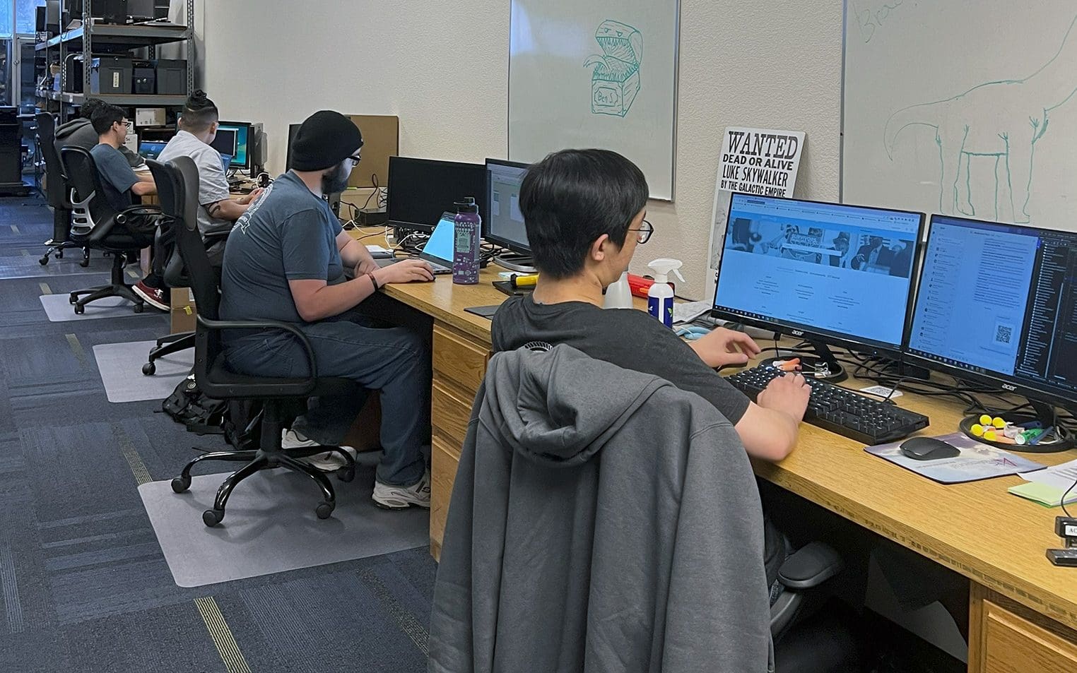 Four PC Professional technicians seated at a row of workstations, each focused on their desktop computers in an office setting