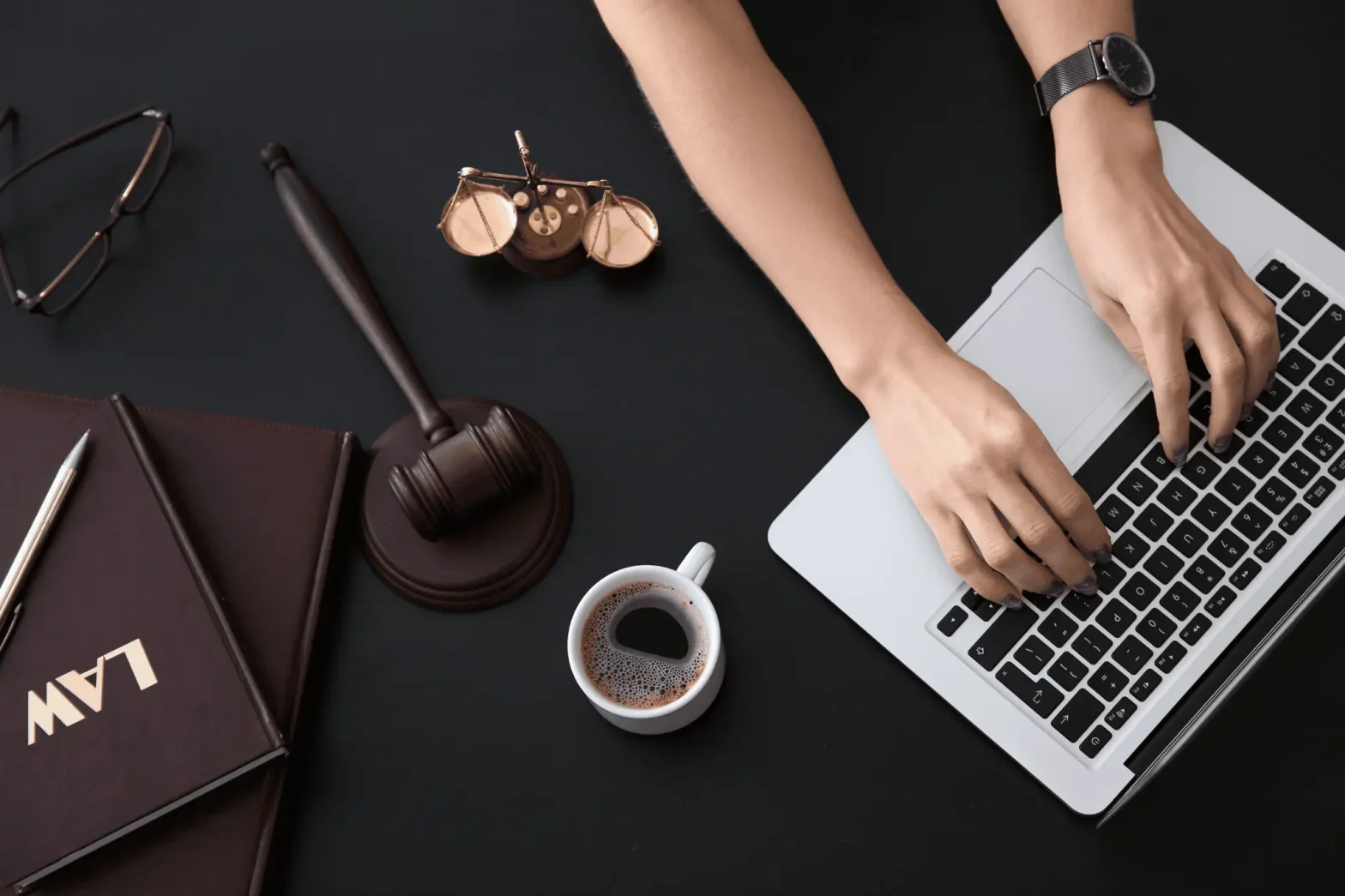 Attorney typing on a laptop beside a gavel, scales, law books, and coffee