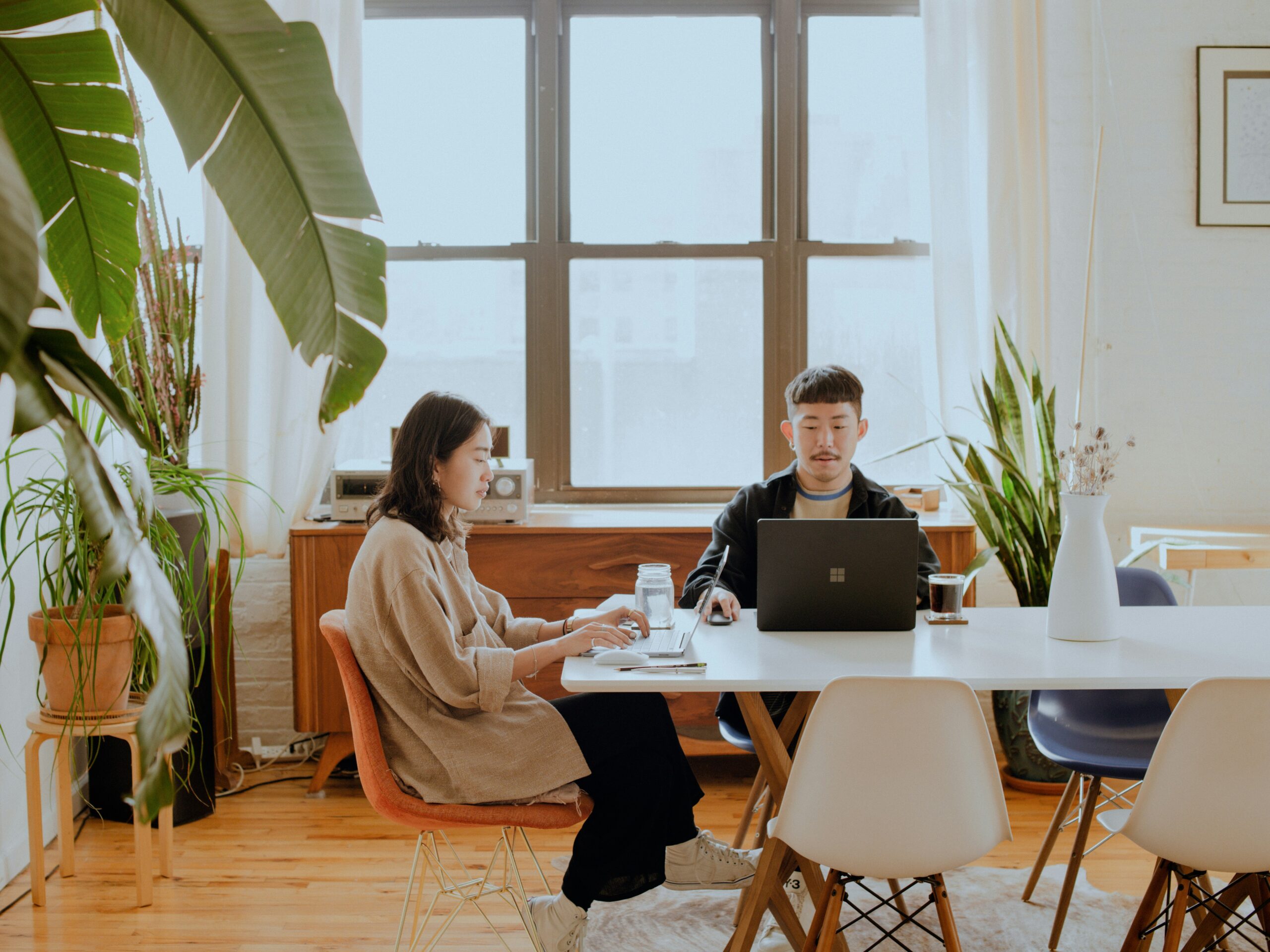 Two people working on their laptops at a shared conference table.