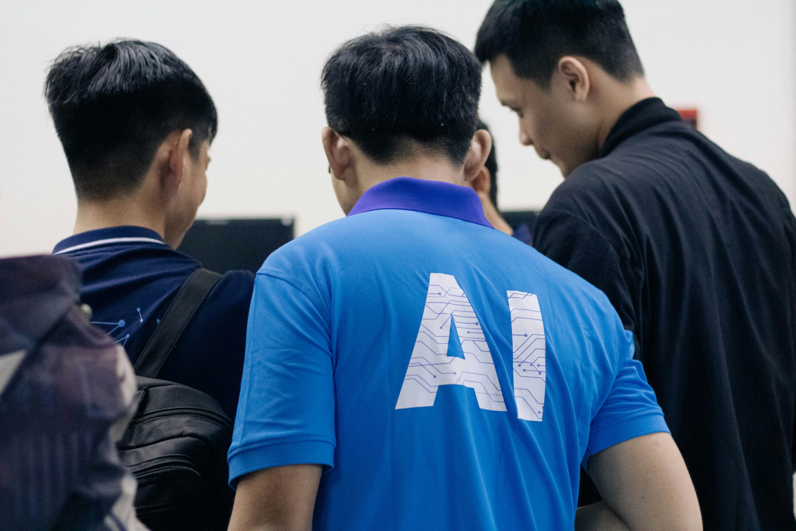 A group of three men talking to another man in a blue shirt with the word "AI" written on the back.