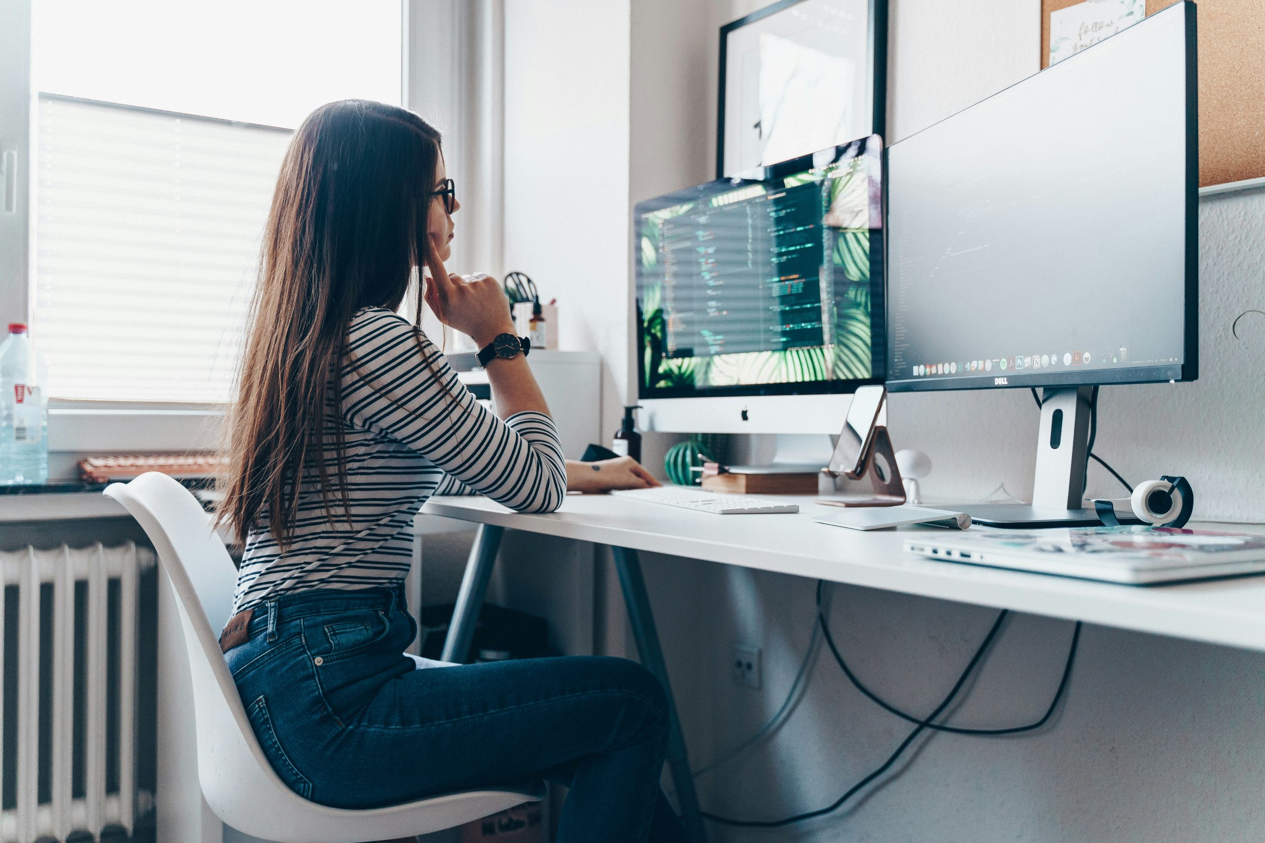 A woman working at her desk, looking at two monitors.